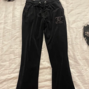 Svarta mjukisbyxor från Juicy Couture - Snygga svarta mjukisbyxor från Juicy Couture med logga på framsidan. Byxorna har en bekväm passform med snörning i midjan och fickor bak. Perfekta för nån som inte är längre än 160 cm!