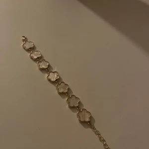LYLA guldarmband med blommotiv  - Jätte fint armband i guld med flera blommor. Varje blomma har en vit insida som ger en fin kontrast mot guldet. Perfekt för att ge en stilfull touch till din outfit. Aldrig använd då jag fick i fel färg 