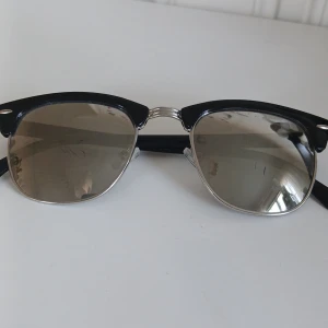 Svarta solglasögon med silverdetaljer - Snygga solglasögon med svart båge och spegelglas. De har en klassisk design med silverdetaljer vid näsbryggan och gångjärnen. Perfekta för en stilren look. Kan finnas några små repor i glaset. Tyvärr har jag ingen ask eller något att lägga dem i men fixar så de intr repas ellee går sönder i frakten. 