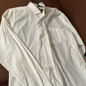 Vit skjorta från Kaplen - Säljer en klassisk vit skjorta från Kaplen i storlek XXL. Skjortan har långa ärmar och en bröstficka. Perfekt för en stilren look. Tillverkad i ett lätt och bekvämt material.