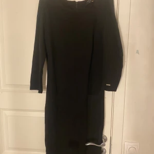 Svart klänning med trekvartsärm - Elegant svart klänning med trekvartsärm och en stilren design. Perfekt för en sofistikerad look. Klänningen har en diskret dragkedja i ryggen för enkel påklädning.