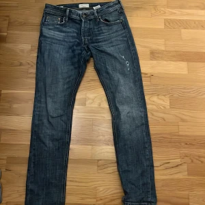 Blå jeansbyxor - Säljer ett par klassiska blå jeansbyxor med en lätt slitningseffekt. De har en knappgylf och femficksdesign. Perfekta för en avslappnad stil. Modellen är slim glenn!