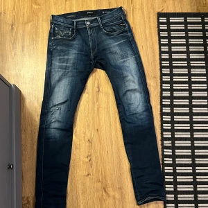 Blå jeans från Replay - Säljer ett par snygga blå Replay Hyperflex Anbass jeans med slitningar. De har en klassisk femficksdesign med dragkedja och knapp. Jeansen har en modern passform och är perfekta för en avslappnad stil. Dem är i storlek 31/34 men passar som 31/32 på mig som är 183 och väger 71 kg. Det är bara att höra av sig vid funderingar🤗