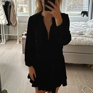 Svart sammetsklänning från Zara - Säljer en elegant svart sammetsklänning från Zara. Klänningen har långa ärmar och en v-ringad design med en knytning i midjan som ger en fin siluett. Perfekt för en stilren look. Storlek XS. Mycket bra skick och väldigt skön. Stretchig i materialet. Den har knappar längs hela vägen så man kan knäppa hela vägen upp istället för att ha den v-ringad. nypris var 499kr