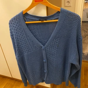 Blå stickad kofta från Mango - Säljer en blå stickad kofta från Mango med v-ringning och knappar framtill. Koftan har en fin strukturstickning och långa ärmar. Perfekt för kyliga dagar!