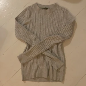 Beige ribbad tröja - Säljer en stilren beige ribbad tröja med långa ärmar. Perfekt för kyligare dagar och lätt att matcha med olika outfits. Tröjan har en klassisk rund halsringning och är gjord i ett mjukt material.