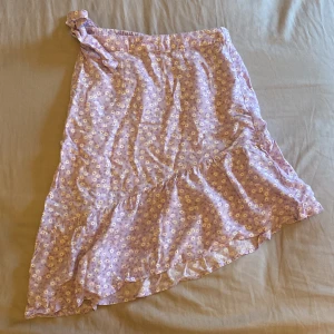 Lila blommig kjol från KappAhl - Söt lila kjol från KappAhl med blommigt mönster och volangdetaljer. Kjolen har en omlott-design och knytning i midjan, vilket ger en fin passform. Perfekt för varmare dagar!💓