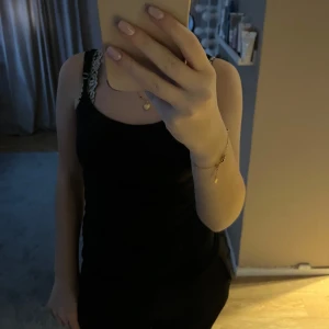 Svart ärmlös klänning - Elegant svart ärmlös klänning med spetsdetaljer vid axlarna. Perfekt för en stilren look. Svart tajt linne från Vera Moda