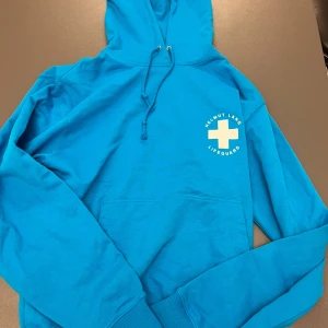 Blå hoodie från Helmut Lang - Snygg blå hoodie från Helmut Lang med texten 'Lifeguard' och ett kors på framsidan. Baksidan har ett unikt tryck med olika knutar och texten 'A Visual Aid for Summer 2022'. Perfekt för en avslappnad stil.