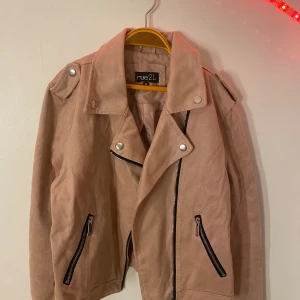 Beige mockajacka från rue21 - Snygg beige mockajacka från rue21 med dragkedja och knappar. Jackan har en klassisk bikerstil med långa ärmar och två dragkedjefickor framtill. Perfekt för en trendig look.