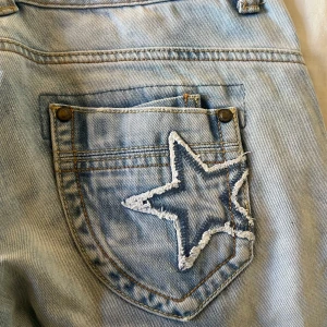 Ljusblå jeans från MOD - Snygga ljusblå jeans från MOD med en cool stjärndetalj på bakfickan. De har en klassisk femficksdesign och en knappgylf. Perfekta för en avslappnad stil. 27/32
