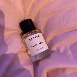 ESSNCE Dusty Amber Eau de Parfum - Säljer en elegant flaska med ESSNCE Dusty Amber Eau de Parfum. Flaskan är genomskinlig med en stilren vit etikett och svart text. Den har en svart kork och rymmer en doft som ger en känsla av mystik och värme. Säljer pga vill köpa en annan doft, (använd 1 sprut). Nypris: 350 (390 med frakt). Säljer för 300kr