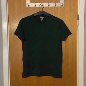 Mörkgrön t-shirt från H&M - Säljer en mörkgrön slim fit t-shirt från H&M. Perfekt för en stilren och enkel look. T-shirten är kortärmad och tillverkad i ett mjukt material som ger en bekväm passform.
