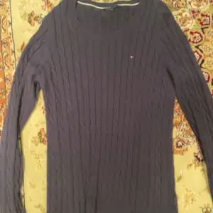 Säljer en stilren mörkblå stickad tröja från Tommy Hilfiger. Tröjan har ett klassiskt flätmönster och långa ärmar. Perfekt för kyligare dagar. Junior storlek. Klassisk. Passar för allt möjligt