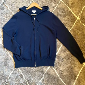 Kashmir hoodie med dragkedja - Säljer en stilren mörkblå hoodie. Tröjan har en praktisk dragkedja framtill och en bekväm huva med snörning. Perfekt för kyliga dagar. Gjord av det dyra meterialet Kashmir.