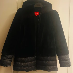 Svart jacka från Guess - Snygg svart jacka från Guess med dragkedja och pufferdetaljer längst ner. Jackan har en mjuk, pälsliknande textur upptill och är perfekt för kyligare dagar. Den har långa ärmar och en stilren design.