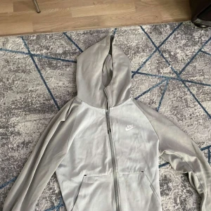 Grå hoodie och byxor från Nike - Säljer en grå hoodie och matchande byxor från Nike. Hoodien har dragkedja och långa ärmar, medan byxorna har elastisk midja och sidofickor. Perfekt för en avslappnad stil.