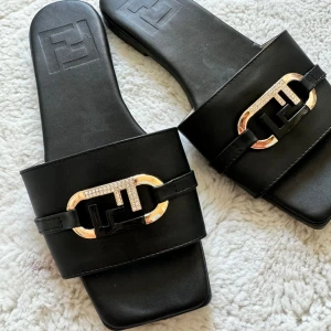 Svarta sandaler med metallspänne - Stilrena svarta sandaler med fyrkantig tå och ett elegant metallspänne i guldton. Perfekta för en avslappnad men chic look.
