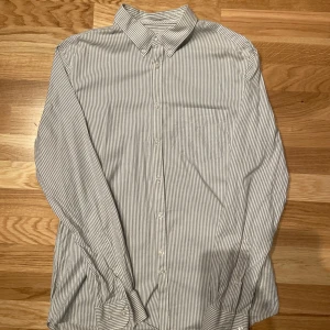 Randig skjorta från J.Lindeberg - Snygg randig skjorta från J.Lindeberg i slim fit. Skjortan har långa ärmar och knappar framtill. Perfekt för en stilren look. Vi grå randig.