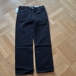 Svarta jeansbyxor från Just Junkies - Snygga svarta jeansbyxor från Just Junkies i modellen 'Wider Black'. Byxorna har en rak passform och är tillverkade av 100% bomull. Perfekta för en stilren look med klassiska femficksdetaljer och knappgylf.
