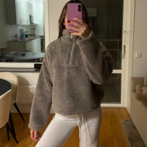 Teddyflis - Mysig beige fliströja med dragkedja och hög krage. Perfekt för kyliga dagar med sin fluffiga och varma design. Den har långa ärmar och en avslappnad passform. Går att justera midjan (bild 2), funkar som jacka. Storlek S