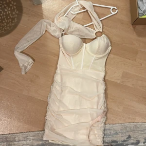 Champagnefärgad klänning med halterneck - Snygg champagnefärgad klänning med halterneck och vadderade kupor. Den har en tight passform och är gjord i ett glansigt material. Perfekt för festliga tillfällen! Klänningen har en dragkedja i ryggen och rynkade detaljer längs sidorna.