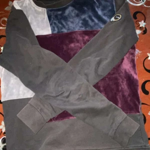 Flerfärgad tröja från Avichy - Säljer en snygg flerfärgad tröja från Avichy. Den har en cool blockdesign i svart, blått, lila och vitt. Materialet ser ut att vara mjukt och lite glansigt, perfekt för en chill dag. Tröjan har långa ärmar och en normal passform. Perfekt för höst och vinter!