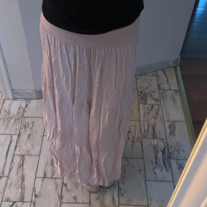 Ljusrosa långkjol - Säljer en superfin ljusrosa långkjol som är perfekt för sommardagar. Kjolen har en bekväm resår i midjan och ett luftigt fall. Den är gjord i ett lätt och skönt material som passar både till vardags och fest. Perfekt att matcha med en enkel topp eller blus! Använder inte då den är lite kort för mig. Är 177cm men passar 170 och kortare