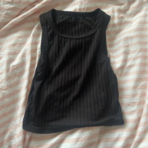 Svart ribbad linnetopp - Säljer en snygg svart ribbad linnetopp. Toppen är ärmlös och har en tight passform som framhäver figuren. Den är gjord i ett mjukt och stretchigt material som är bekvämt att bära hela dagen. Säljer pga att den inte kommer till användning <3