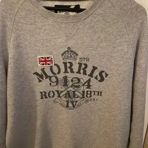 Säljer en snygg grå sweatshirt från Morris med tryck av brittiska flaggan och text. Perfekt för en casual look. Tröjan är i bra skick och passar perfekt för höst och vår. Den har en normal passform och är superbekväm. Perfekt för dig som gillar stilrena plagg med en touch av brittisk elegans.