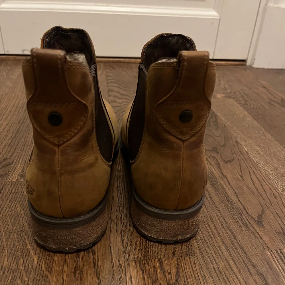 Säljer ett par snygga bruna boots från UGG i skinn. De har en klassisk design med elastiska paneler på sidorna för enkel på- och avtagning. Perfekta för höst och vinter med en robust sula som ger bra grepp. Använda men i bra skick, redo för nya äventyr!. Skor.