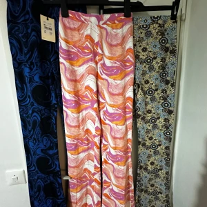 Färgglada byxor från Bik Bok helt nya - Säljer tre par färgglada byxor från Bik Bok i storlek XS. Ett par har ett psykedeliskt mönster i rosa, orange och vitt. De andra är blå med ett abstrakt mönster och ett par med blommigt mönster i brunt och blått. Perfekta för att liva upp garderoben! Total kostar dem 850kr men jag säljer dem för 500kr