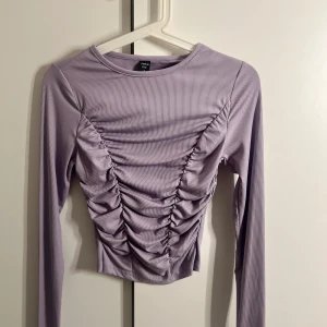 Stilig Lila Topp 💜 - Säljer en superfin lila ribbad topp från  SHEIN Den har långa ärmar och en snygg rynkad detalj framtill som ger en cool look. Perfekt för både vardag och fest! 💜