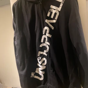 Svart hoodie med text - Säljer en svart hoodie med texten 'UNSTOPPABLE' i vitt på framsidan. Den har en dragkedja och är långärmad, perfekt för en casual look. Materialet känns mjukt och bekvämt, idealiskt för höst och vår. Passar bra till både träning och vardagsbruk.