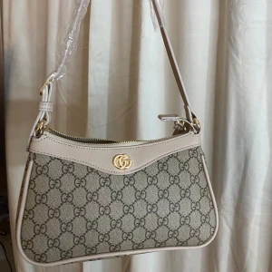 Väska - Säljer en snygg inspirerad beige axelväska i mycket bra skick. Väskan är gjord i ett slitstarkt material med läderdetaljer. Den har en dragkedja upptill och en justerbar axelrem. Har små skråmor på guldet, men inget som syns från avstånd (sista bilden) annars superfin och oanvänd. Perfekt för både vardag och fest! Går ner i pris vid snabb affär🩷