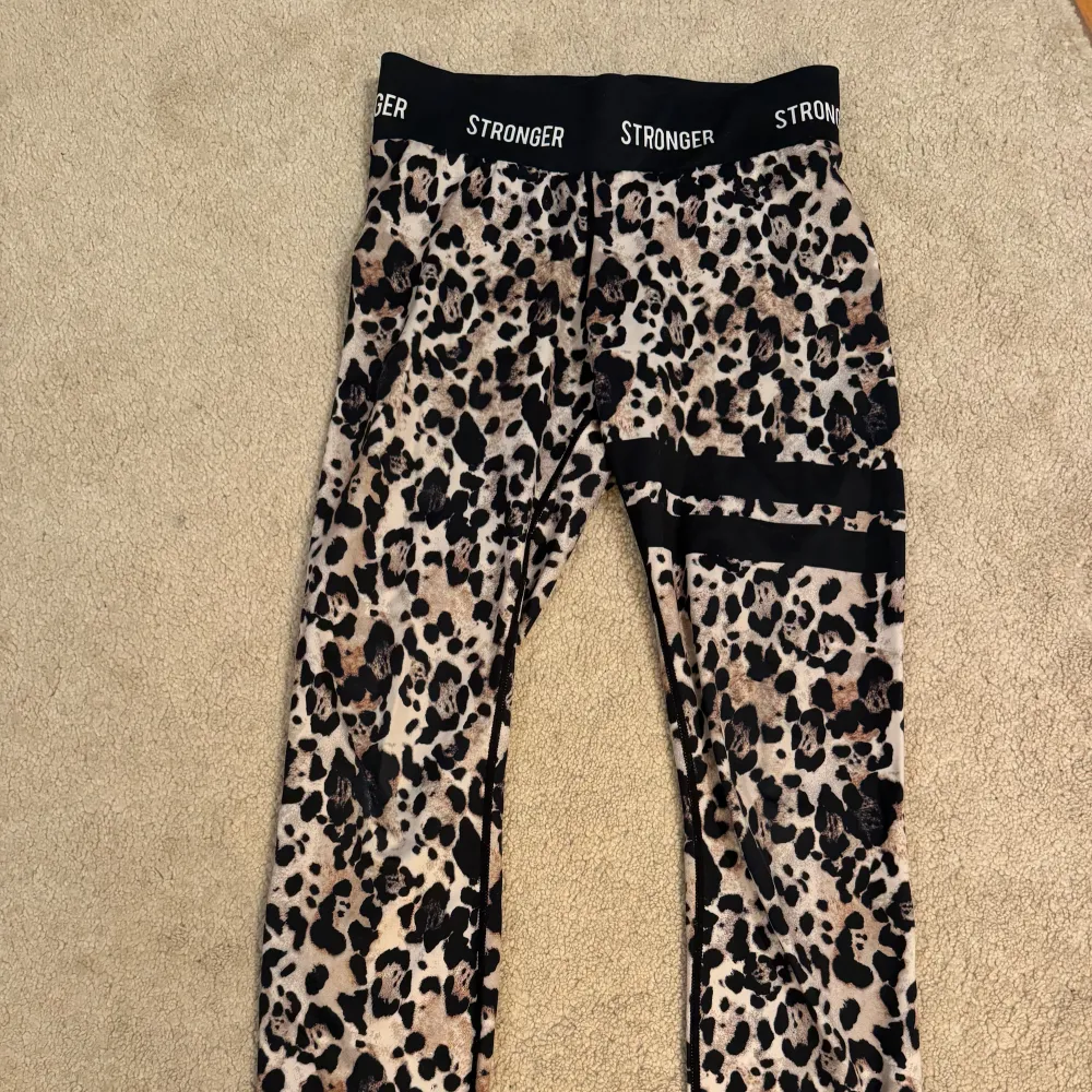 Snygga leopardmönstrade leggings från Stronger. Perfekta för träning eller en cool vardagslook. De har en hög midja och är superstretchiga för bästa komfort. Svarta detaljer med logga runt midjan och på benet ger en extra touch.. Jeans & Byxor.