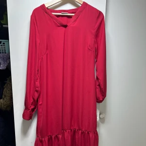 Röd långklänning med volang - Säljer en superfin röd långklänning med volangdetalj längst ner. Klänningen har långa ärmar och en v-ringad hals. Perfekt för höst och vinter, kanske till julfesten! Materialet känns mjukt och bekvämt, troligen polyester. Passar perfekt för en festlig kväll.