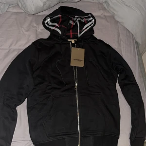 Svart hoodie från Burberry - Säljer en snygg svart hoodie från Burberry i nytt skick. Det är storlek M men den sitter mer som en S. Oanvänd med tags kvar, perfekt nu till hösten/vintern då den är varm. Skriv för frågor. 1.(1) säljer en grå också en för 600 båda för 1000.
