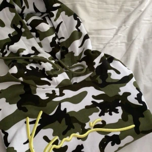 Karl Kani Camouflage hoodie med gul broderad text - Säljer en cool hoodie i camouflage-mönster med en snygg gul broderad text på framsidan. Den har en bekväm passform med långa ärmar och en praktisk huva. Perfekt för en avslappnad stil eller streetwear-look! Helt ny skick, knappt använd.