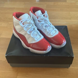 Jordan 11 Cherry Red - Säljer ett par snygga Nike Air Jordans i rött och vitt. Skorna har en cool design med snörning och en hög modell. Perfekta för både vardag och fest! De är i bra skick och kommer i originalkartong.