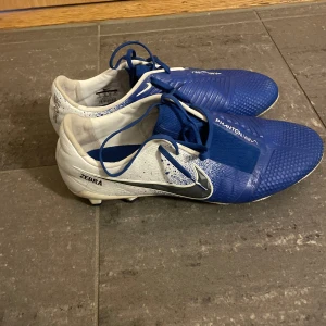 Nike Phantom Vision fotbollsskor - Säljer ett par Nike Phantom Vision fotbollsskor i blått och vitt. Skorna har en cool design med snörning och är perfekta för fotbollsträning. De är i mycket bra skick nästan aldrig använda 