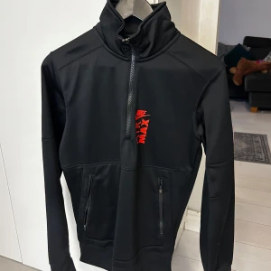 Svart Nike Air Max tröja - Säljer en svart Nike Air Max tröja i Therma-Fit material då jag ej använder den. Perfekt för kyliga dagar med sin höga krage och halv dragkedja. Passar perfekt för träning eller vardagsbruk.