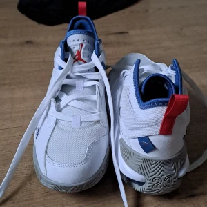 Jordan 23  - Säljer ett par Nike Air Max sneakers i vitt med blå detaljer och en cool röd flik på hälen. De har en snygg design med nummer 23 på sidan och en bekväm sula för extra dämpning. Perfekta för både vardag och träning!