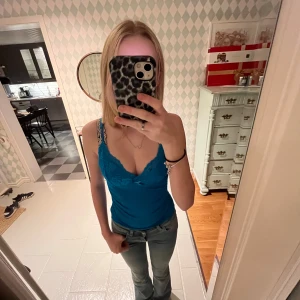 Blå linne med spetsdetaljer - Säljer ett snyggt blått linne med spetsdetaljer vid axelbanden. Perfekt för sommardagar eller som ett lager under en kofta. Linnet har en tight passform och är i mycket bra skick. Passar både till vardags och fest!