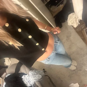 Kofta med guldknappar - Säljer en snygg svart  kofta med iögonfallande guldknappar. Perfekt för en utekväll eller fest! Toppen har korta ärmar, vilket gör den både stilren och trendig. Passar perfekt till jeans eller kjol för en chic look.