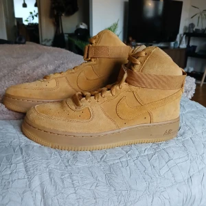 Bruna Nike Air Force i mocka - Säljer ett par snygga bruna Nike Air Force i mocka. De har en hög modell med snörning och en justerbar rem runt ankeln. Perfekta för höst och vår med sin robusta design och bekväma passform. Skorna är i mycket bra skick och redo för nya äventyr! Storlek 38!