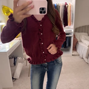 Vinröd kofta med volangdetaljer - Säljer en superfin vinröd kofta med volangdetaljer och pärlknappar. Perfekt för höst och vinter! Den är långärmad och har en mysig passform🥰🥰🥰