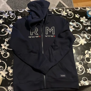 Mörkblå kofta från Race Marine - Säljer en snygg mörkblå kofta från Race Marine i storlek S. Den har en dragkedja framtill och coola vita bokstäver 'RM' på bröstet med koordinater under. Perfekt för höst och vår, och den är i mycket bra skick. Superbekväm och stilren!