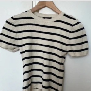 Randig kortärmad topp från Gina Tricot - Säljer en superfin randig topp från Gina Tricot i storlek M. Den är beige med svarta ränder och har korta ärmar. Perfekt för vår och sommar! Toppen är croppad och ger en snygg look till jeans eller kjol. Använd få gånger och i mycket bra skick.