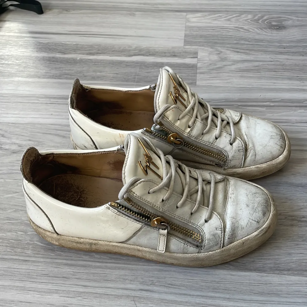 Säljer ett par vita sneakers från Giuseppe Zanotti i skinn. . Skorna är i okej skick men har tydliga tecken på användning, dragkedjornas grej man drar i på insida foten är sönder på båda skor speciellt på sulorna. Men dessa skor man man enkelt tvätta upp och fixa så att de blir fräscha! Priset går att diskuteras!. Skor.